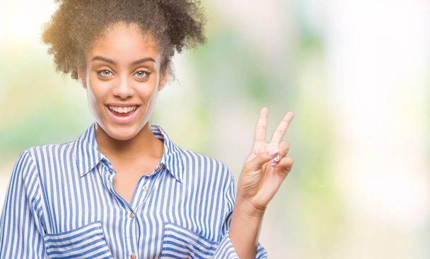 Young afro american woman over isolated background smiling with happy face winking at the camera doing victory sign. Number two. - Photo, Image