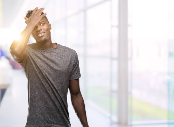 Jonge Afro-Amerikaanse man grijs t-shirt verrast met de hand dragen op hoofd voor fout, niet vergeten fout. Vergat, slecht geheugen concept. - Foto, afbeelding