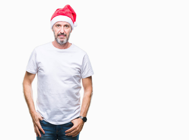 Middle age hoary senior man wearing christmas hat over isolated background with serious expression on face. Simple and natural looking at the camera. - Foto, afbeelding
