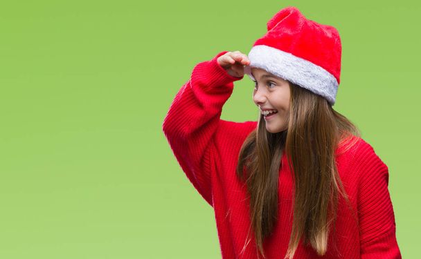 Mladá krásná dívka, která nosí vánoční čepice přes samostatný pozadí velmi šťastný a usmívající se, hledá daleko s rukou přes hlavu. Hledání koncepcí. - Fotografie, Obrázek