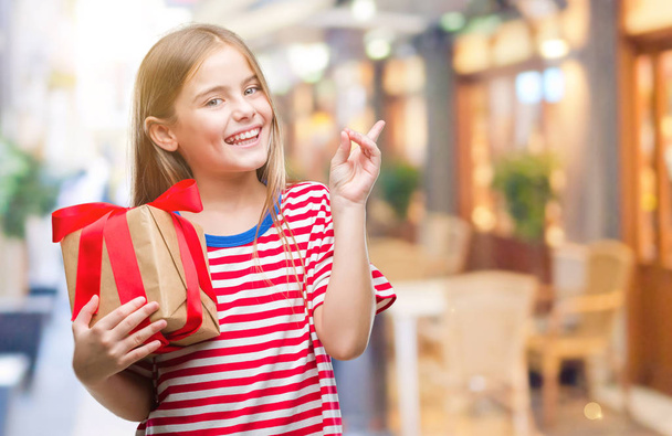 Young beautiful girl giving christmas or valentine gift over isolated background very happy pointing with hand and finger to the side - Фото, изображение