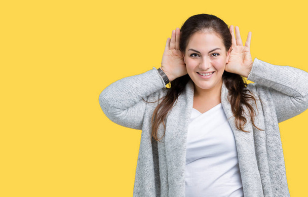 Beautiful plus size young woman wearing winter jacket over isolated background Trying to hear both hands on ear gesture, curious for gossip. Hearing problem, deaf - Photo, Image