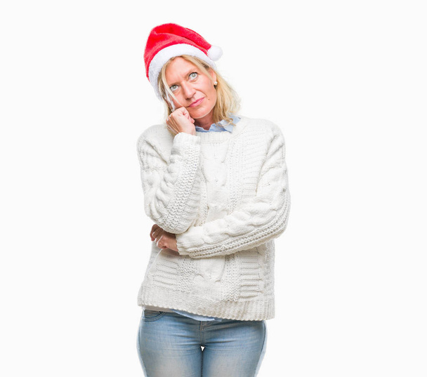 Középkorú szőke nő visel kalapot karácsony több mint elszigetelt háttér kézzel a chin gondolkodás kérdés, töprengő kifejezés. Mosolygós, figyelmes arccal. Kétség koncepció. - Fotó, kép