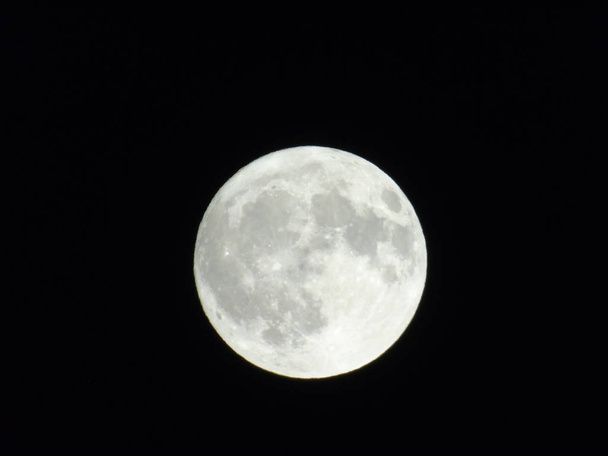 Een geweldige fotografie van het volle maanlicht onder een donkere lucht met enkele kleine sterren op de achtergrond - Foto, afbeelding