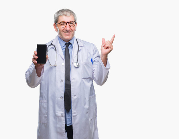 Красавчик старший врач показывает экран смартфона на изолированном фоне очень счастлив указывая рукой и пальцем в сторону
 - Фото, изображение
