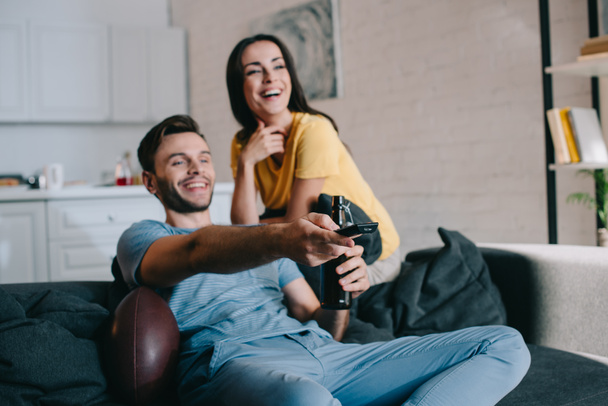 laughing young couple watching american football game at home - Foto, Imagen