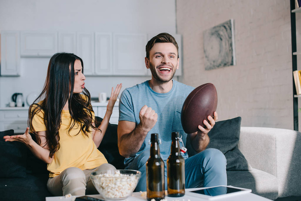 сердита молода жінка кричить на чоловіка, коли він дивиться американський футбол на телебаченні вдома
 - Фото, зображення