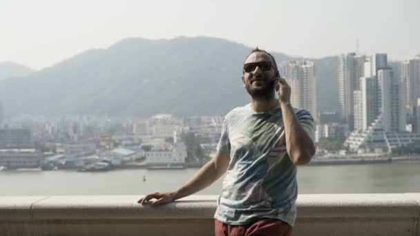 Young man talking on cellphone standing on terrace in city - Video, Çekim