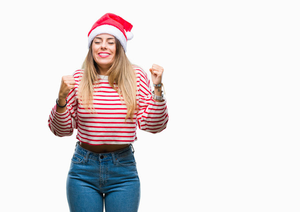 Giovane bella donna indossa cappello di Natale su sfondo isolato molto felice ed eccitato facendo gesto vincitore con le braccia alzate, sorridente e urlando per il successo. Concetto di celebrazione
. - Foto, immagini