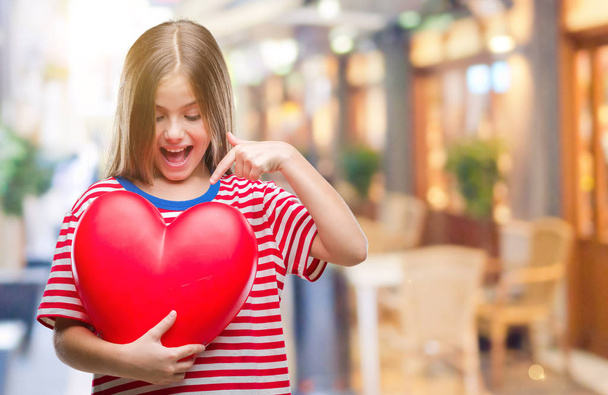 Giovane bella ragazza tenendo il cuore rosso su sfondo isolato molto felice indicando con mano e dito
 - Foto, immagini