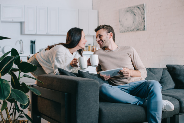 happy young couple with cups of cocoa and tablet relaxing together at home - Foto, Bild