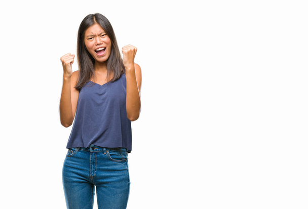 Young asian woman over isolated background very happy and excited doing winner gesture with arms raised, smiling and screaming for success. Celebration concept. - Foto, imagen