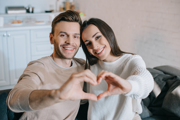 beautiful young couple making heart symbol with hands and looking at camera - 写真・画像