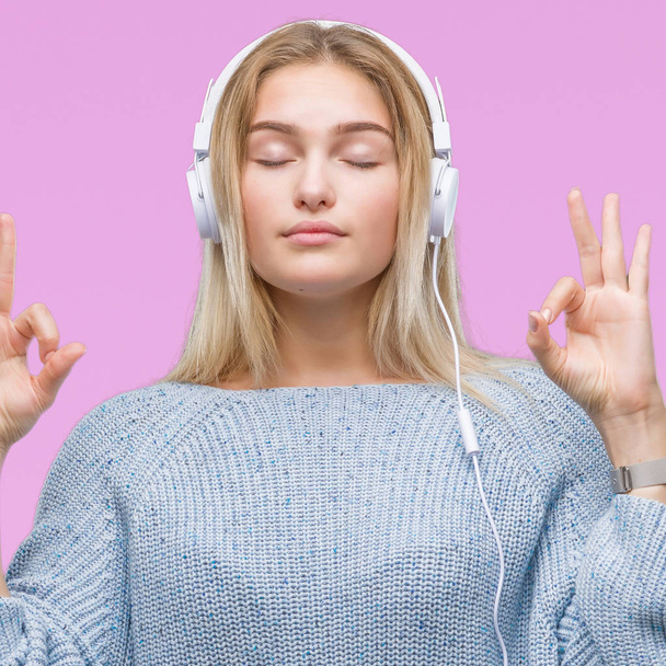 Mujer caucásica joven escuchando música usando auriculares sobre fondo aislado relajarse y sonreír con los ojos cerrados haciendo gesto de meditación con los dedos. Concepto de yoga
. - Foto, imagen