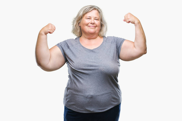 Senior plus grootte Kaukasische vrouw over geïsoleerde achtergrond armen spieren glimlachend trots tonen. Fitness concept. - Foto, afbeelding