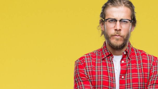 Young handsome man with long hair wearing glasses over isolated background skeptic and nervous, disapproving expression on face with crossed arms. Negative person. - Foto, afbeelding