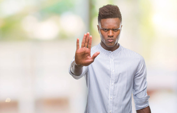 Młody człowiek african american na białym tle robi stop śpiewać z dłoni. Ostrzeżenie wyrażenie z negatywnych i poważne gest na twarzy. - Zdjęcie, obraz