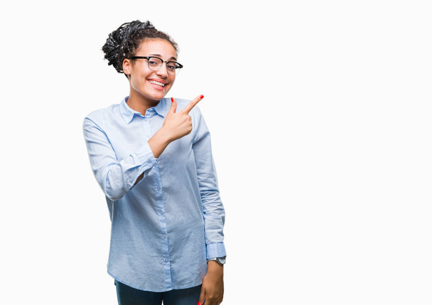 Young braided hair african american business girl wearing glasses over isolated background cheerful with a smile of face pointing with hand and finger up to the side with happy and natural expression on face looking at the camera. - Photo, Image
