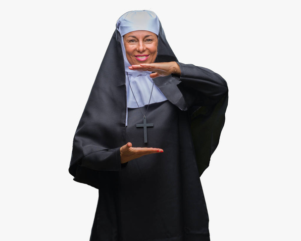 Middle age senior christian catholic nun woman over isolated background gesturing with hands showing big and large size sign, measure symbol. Smiling looking at the camera. Measuring concept. - Foto, imagen