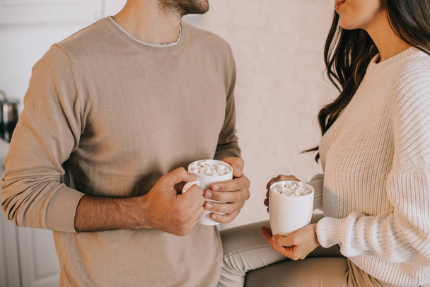 cropped shot of young couple holding mugs of cocoa with marshmallow - Foto, immagini