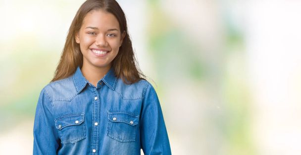 Young beautiful brunette woman wearing blue denim shirt over isolated background with a happy and cool smile on face. Lucky person. - Foto, Bild