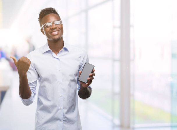 Jovem homem afro-americano usando smartphone apontando com a mão e o dedo para cima com o rosto feliz sorrindo
 - Foto, Imagem