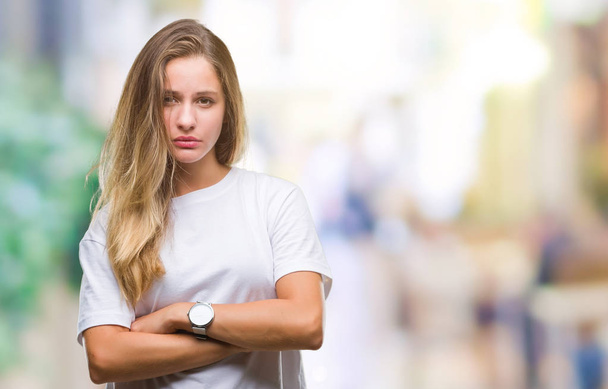 Young beautiful blonde woman wearing casual white t-shirt over isolated background skeptic and nervous, disapproving expression on face with crossed arms. Negative person. - Фото, зображення