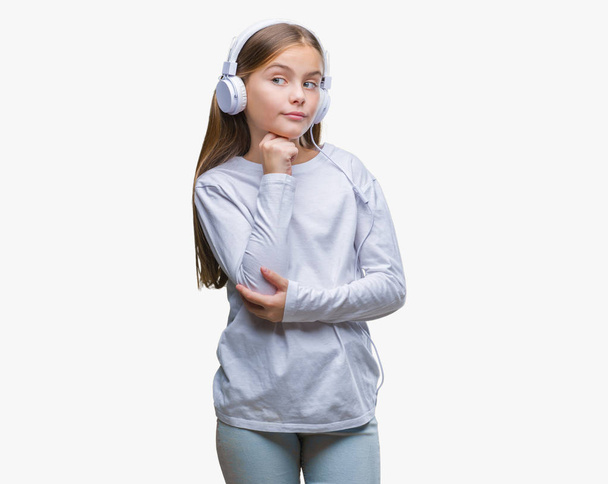 Young beautiful girl wearing headphones listening to music over isolated background with hand on chin thinking about question, pensive expression. Smiling with thoughtful face. Doubt concept. - 写真・画像