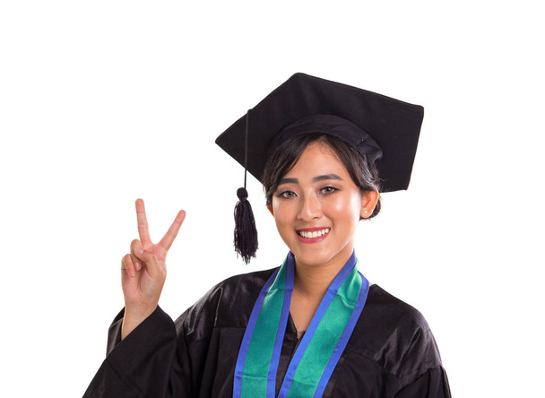Portrait rapproché d'une jeune étudiante asiatique souriante célébrant sa graduation, faisant poser la victoire avec sa main. Plan studio, isolé sur fond blanc
 - Photo, image