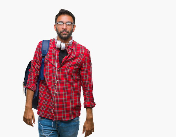 Adult hispanic student man wearing headphones and backpack over isolated background with serious expression on face. Simple and natural looking at the camera. - Φωτογραφία, εικόνα