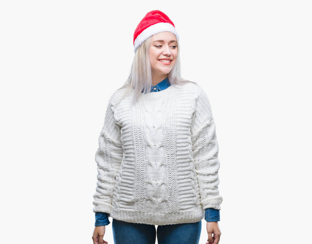 Młoda blond kobieta kapeluszu Boże Narodzenie nad na białym tle, tło patrząc od strony z uśmiechem na twarzy, naturalny wyraz. Śmiejąc się pewnie. - Zdjęcie, obraz
