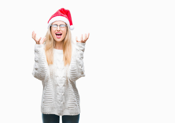 Jovem mulher loira bonita vestindo chapéu de Natal sobre fundo isolado louco e louco gritando e gritando com expressão agressiva e braços levantados. Conceito de frustração
. - Foto, Imagem