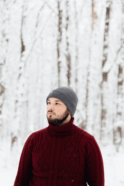 guy in a red knitted sweater and jeans holding a phone, standing on the snow in the winter forest - Foto, Imagen