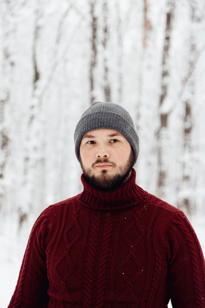 tipo en un suéter de punto rojo y jeans sosteniendo un teléfono, de pie sobre la nieve en el bosque de invierno
 - Foto, Imagen
