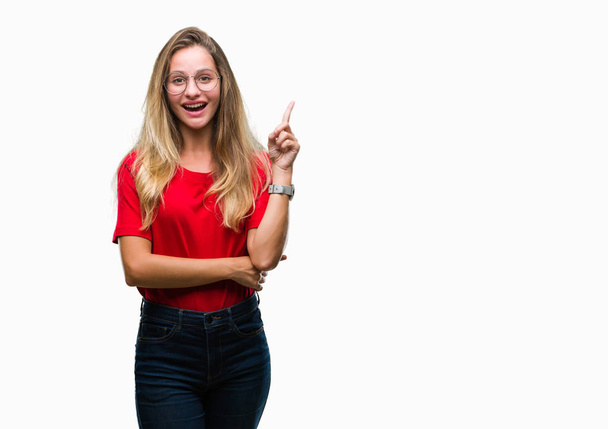 Young beautiful blonde woman wearing glasses over isolated background pointing finger up with successful idea. Exited and happy. Number one. - Photo, Image