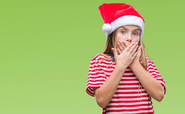 Молодая красивая девушка в рождественской шляпе на изолированном фоне шокировала закрывая рот руками за ошибку. Секретная концепция
. - Фото, изображение