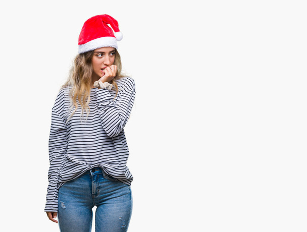 Kaunis nuori blondi nainen yllään joulu hattu yli eristetty tausta näyttää stressaantunut ja hermostunut kädet suulla puree kynnet. Ahdistuneisuusongelma
. - Valokuva, kuva