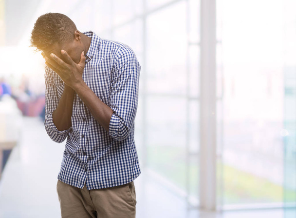 Młody człowiek african american na sobie niebieską koszulę z smutny wyrażenie obejmujące twarz rękami podczas płaczu. Koncepcja depresji. - Zdjęcie, obraz