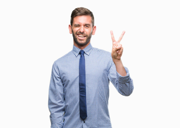 Young handsome business man over isolated background smiling with happy face winking at the camera doing victory sign. Number two. - 写真・画像