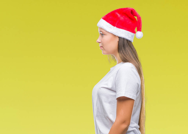 Joven hermosa mujer caucásica con sombrero de Navidad sobre fondo aislado mirando a un lado, pose de perfil relajado con cara natural con sonrisa confiada
. - Foto, Imagen