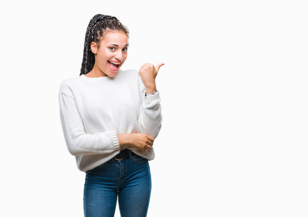 Плетені молодих афро-американських дівчата волосся носити взимку светр над ізольованих фон посміхається з щасливим обличчям, дивлячись і вказуючи на сторону з великим пальцем. - Фото, зображення