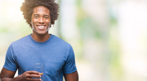 Afro-amerikai ember iszik pohár vizet-elszigetelt háttérhez képest-boldog arccal állt, és mosolyogva, magabiztos mosollyal mutatja a fogak - Fotó, kép