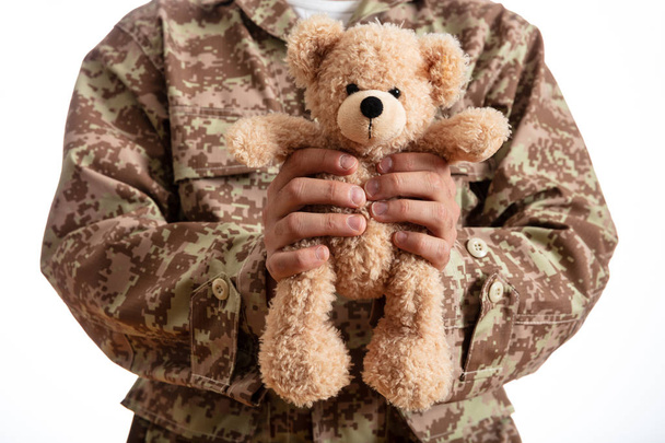 Батька в армії. Молодий солдат тримає плюшевого ведмедика стоячи на білому тлі - Фото, зображення