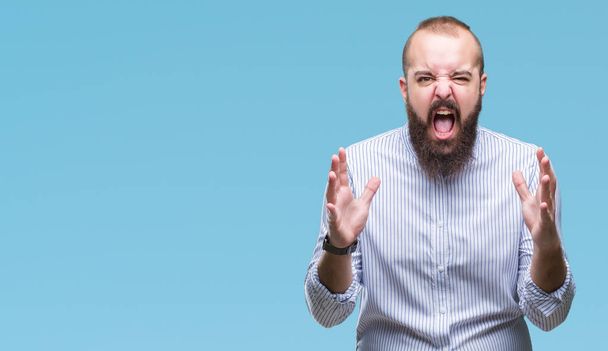 Young caucasian hipster man over isolated background crazy and mad shouting and yelling with aggressive expression and arms raised. Frustration concept. - Fotoğraf, Görsel