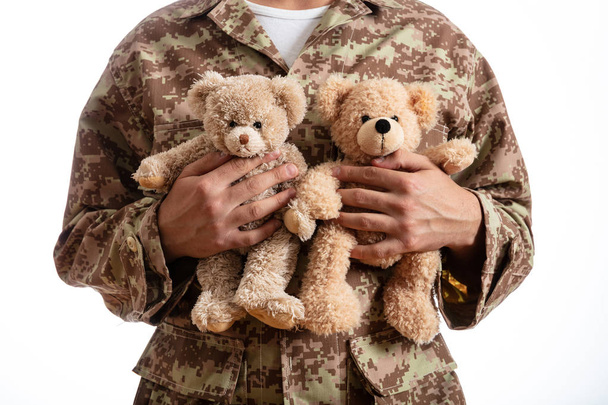 Padre en el ejército. Joven soldado sosteniendo dos osos de peluche de pie sobre fondo blanco
 - Foto, imagen