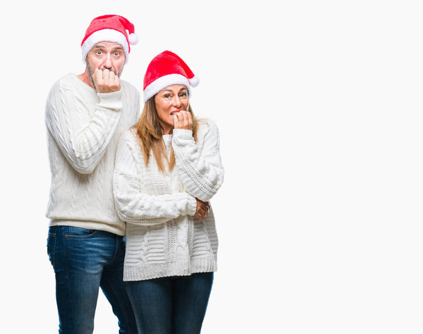 Латиноамериканская пара средних лет в рождественской шляпе на изолированном фоне выглядит напряженной и нервной с руками во рту, грызущими ногти. Проблема тревоги
. - Фото, изображение