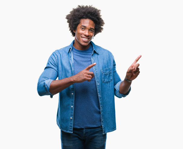 Αφρο αμερικανικό άνθρωπος πέρα από το απομονωμένο υπόβαθρο χαμογελώντας και εξετάζοντας τη φωτογραφική μηχανή κατάδειξης με δύο χέρια και τα δάχτυλα στο πλάι. - Φωτογραφία, εικόνα