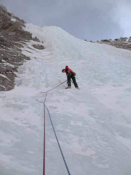 escalador de gelo de montanha masculino escalando uma cachoeira íngreme e longa congelada nos Alpes suíços no inverno profundo
 - Foto, Imagem