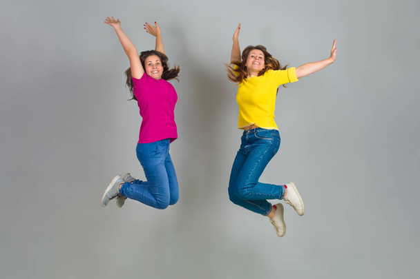 Dos hermanas gemelas saltando sobre fondo gris
 - Foto, imagen