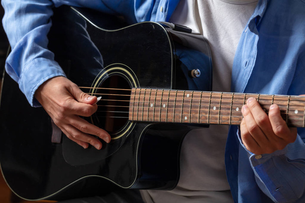 Young man playing guitar, close up view, dark background - Photo, Image